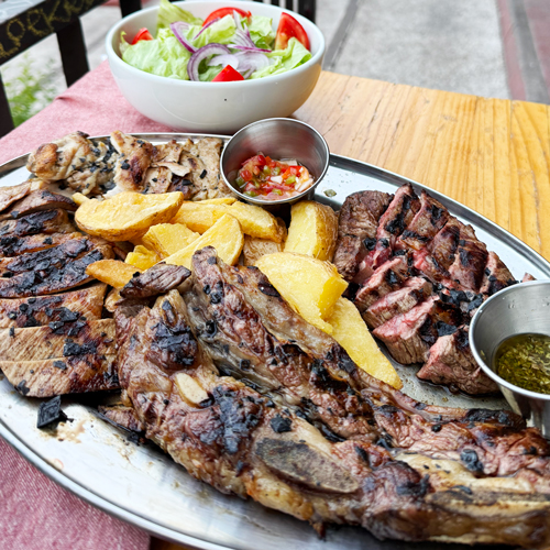 Parrillada de carnes a la brasa con patatas y salsas en bandeja de acero